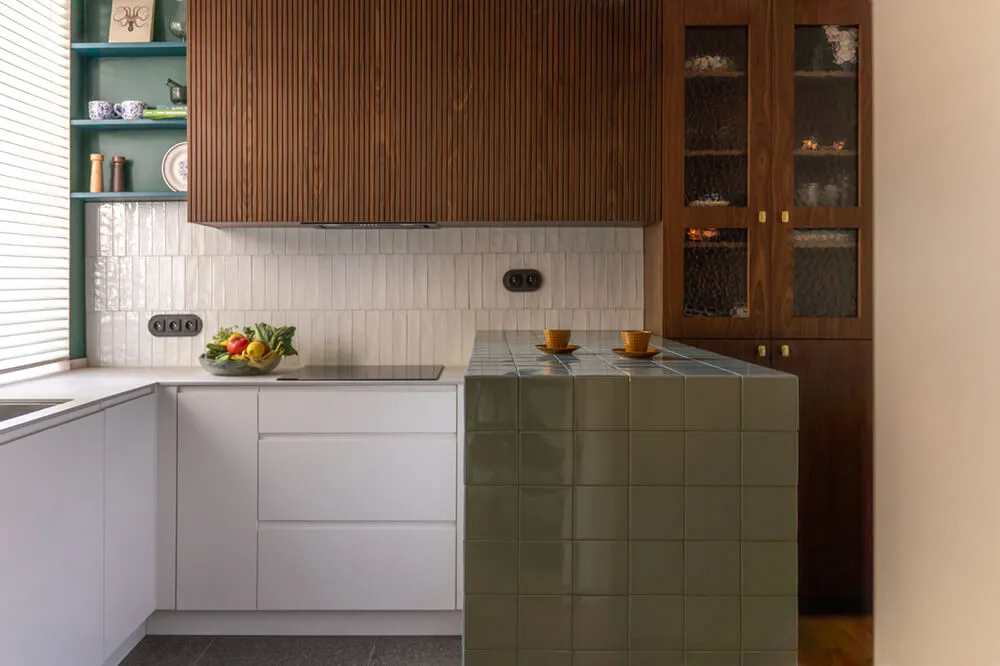 Nowoczesna kuchnia z białymi szafkami, zielonym blatem wyłożonym płytkami i ciemnymi drewnianymi szafkami.