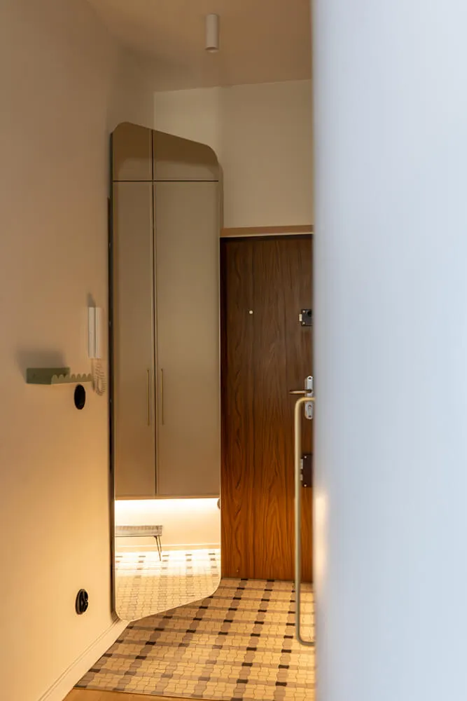 Wnętrze korytarza z drewnianymi drzwiami, dużą szafą z lustrem i geometryczną podłogą.