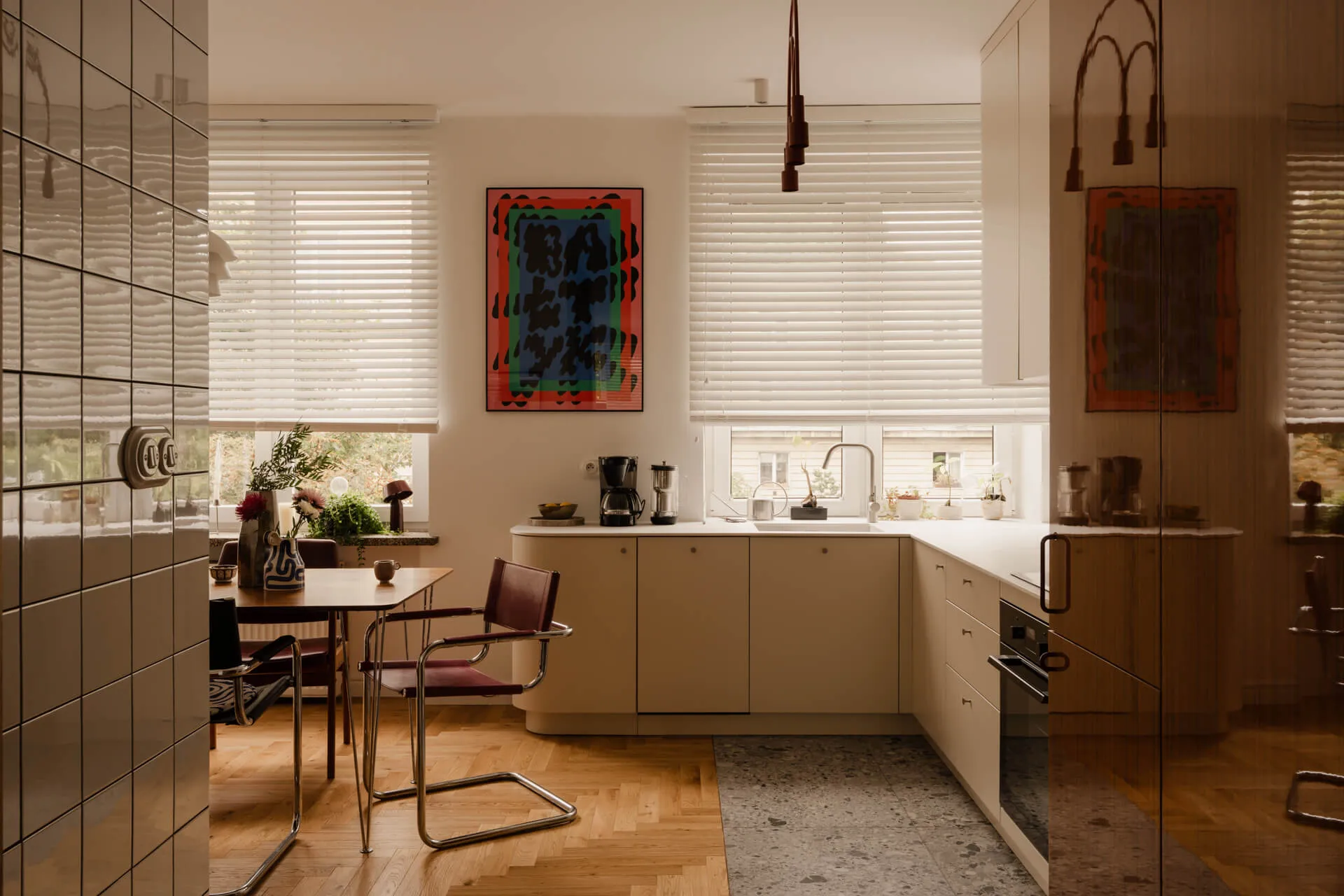 Nowoczesna kuchnia z białymi szafkami, stołem z krzesłami i zasłoniętymi roletami oknami, z widokiem na rośliny.