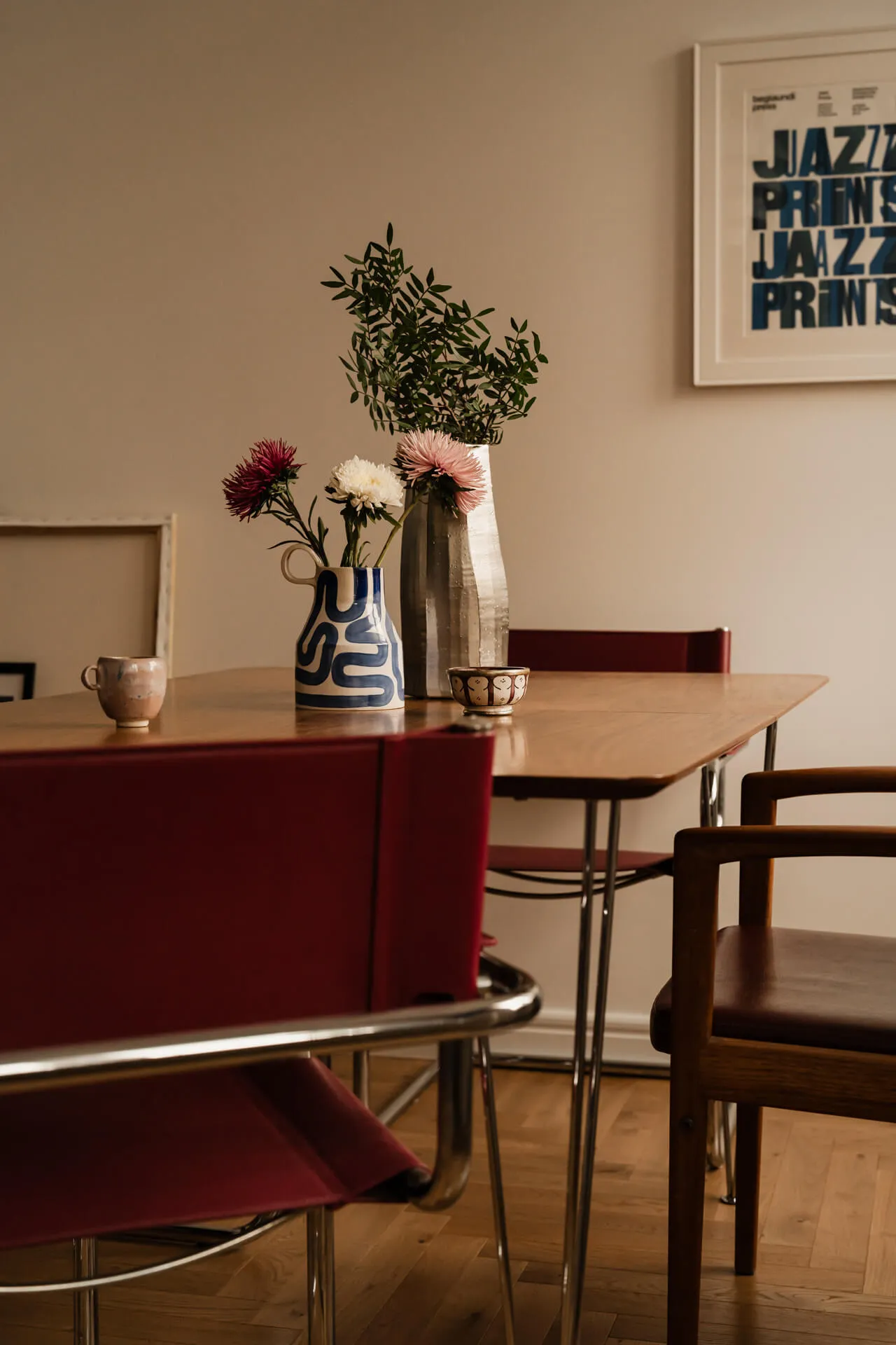 Stół jadalny z czerwonymi krzesłami, dwoma wazonami z kwiatami i zielonymi gałązkami oraz filiżanką i małą miseczką.