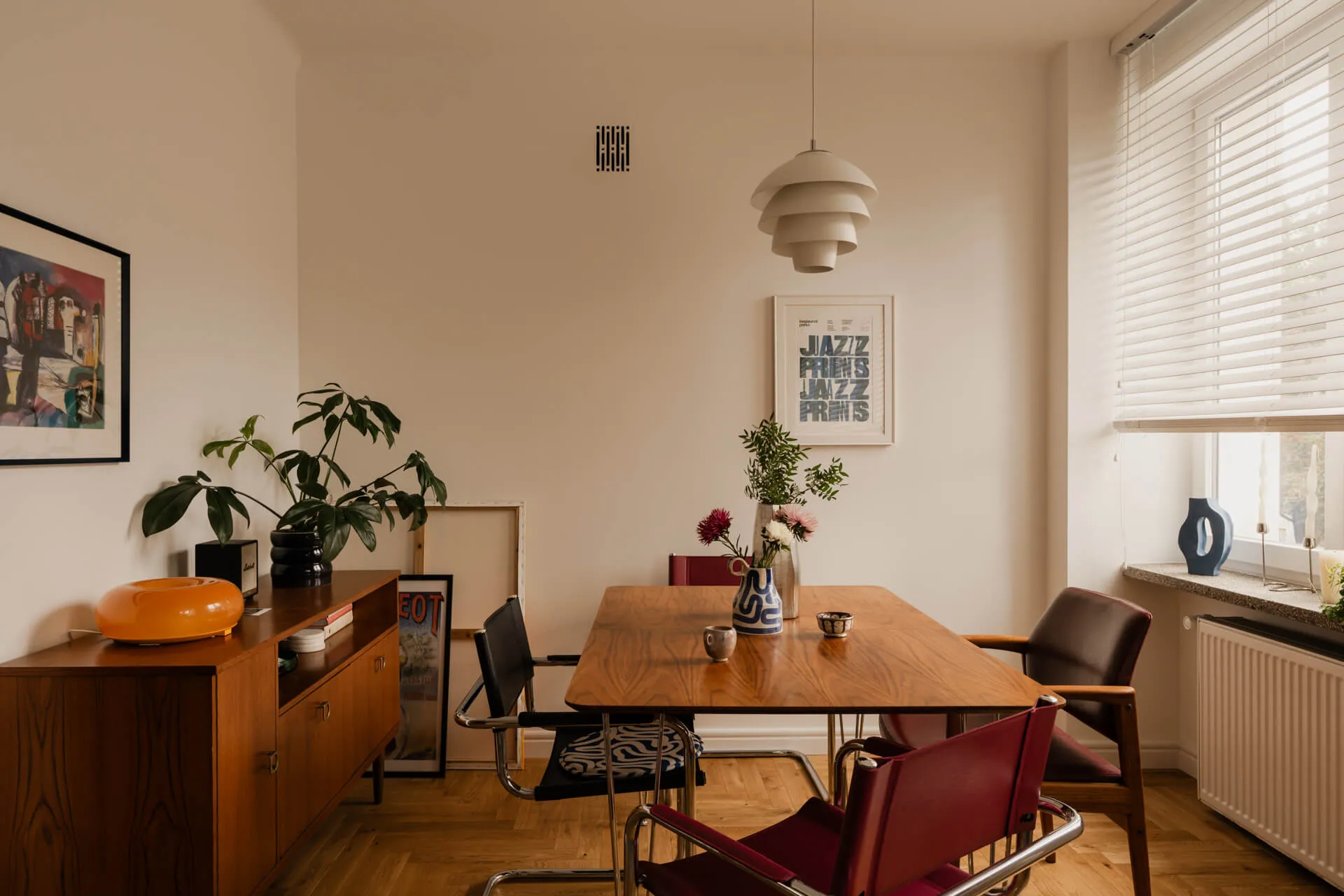 Jadalnia z drewnianym stołem, krzesłami w stylu vintage, kwiatami w wazonach i dekoracjami na białych ścianach.