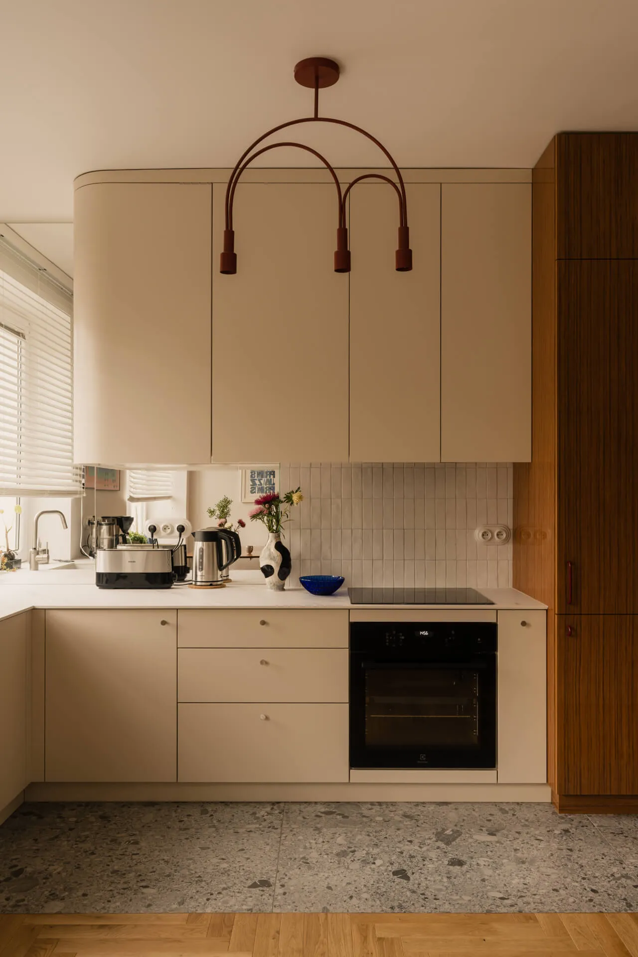 Nowoczesna kuchnia z białymi szafkami, czarnym piekarnikiem, czajnikiem i kwiatami w wazonie na blacie.