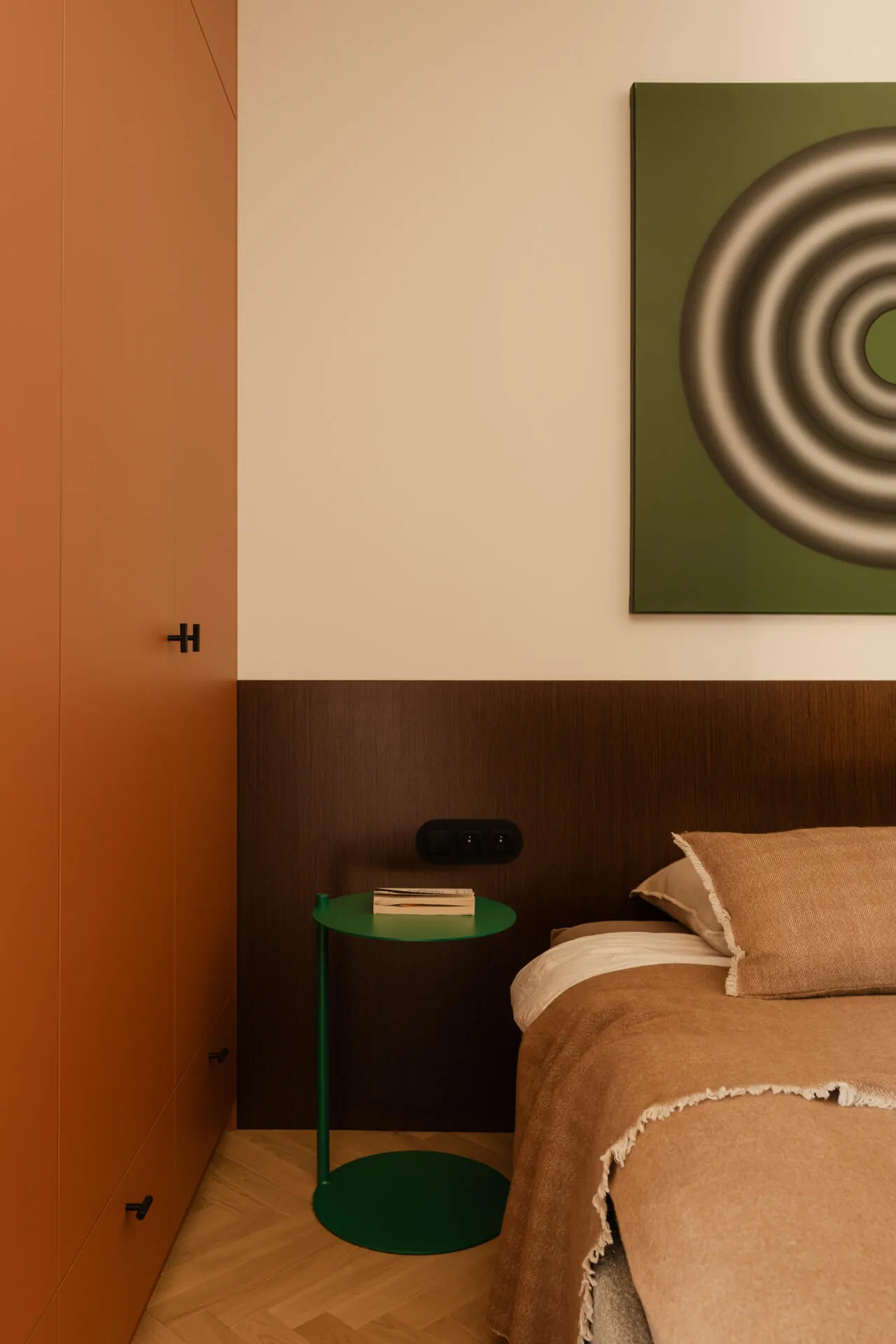 Narożnik sypialni z pomarańczową szafą, zielonym stolikiem nocnym i łóżkiem z brązową narzutą i poduszką.