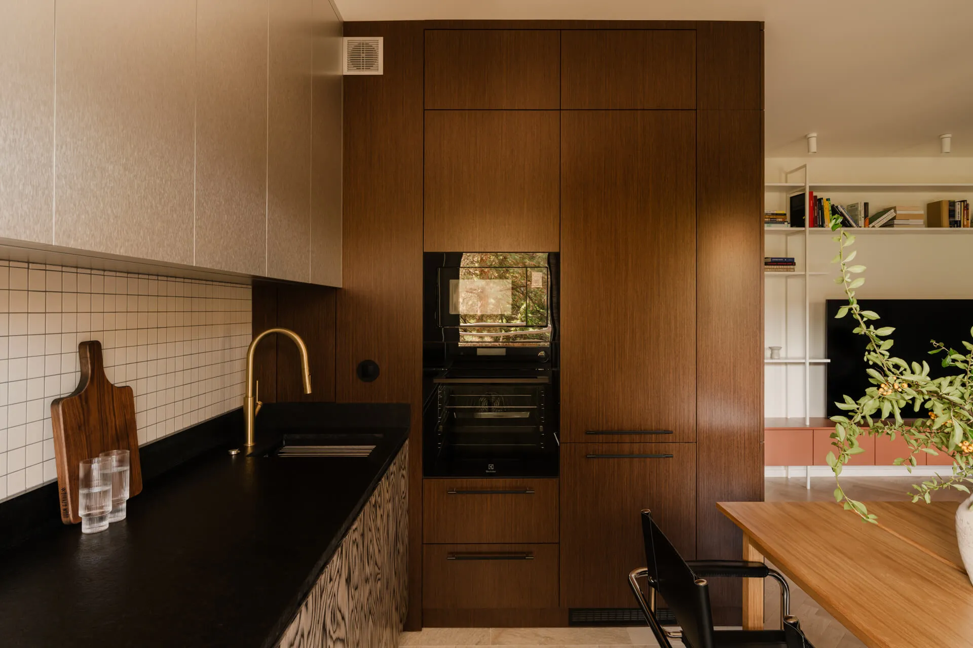 Nowoczesna kuchnia z drewnianymi szafkami, czarnym blatem, złotą baterią i czarnym piekarnikiem wbudowanym.