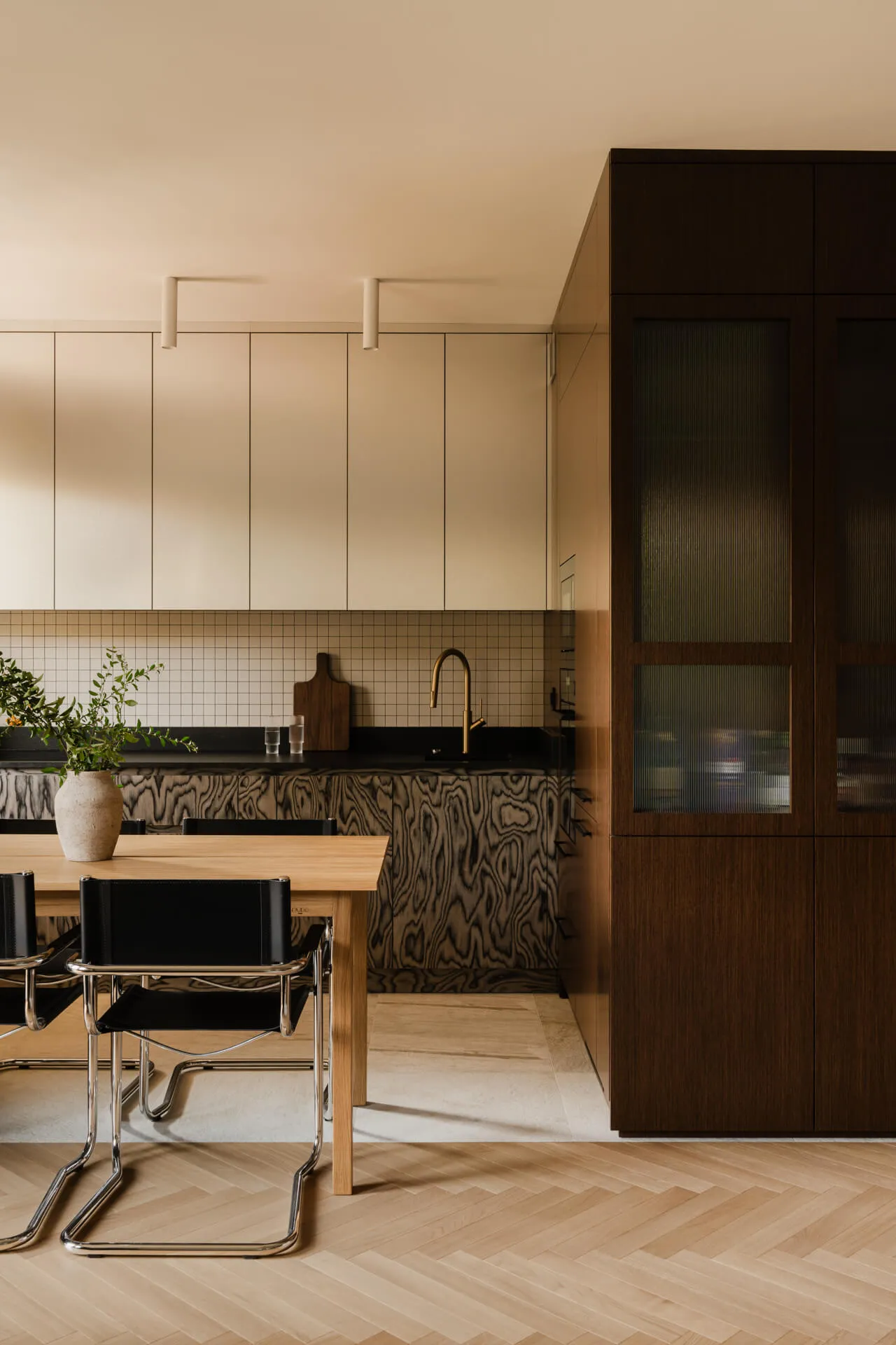 Nowoczesna kuchnia z drewnianym stołem, czarnymi krzesłami, białymi szafkami i ciemnym blatem z unikalnym wzorem drewna.