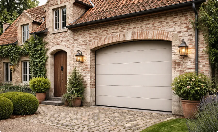 Maison en briques avec une porte en bois, un garage blanc et des plantes en pots autour.