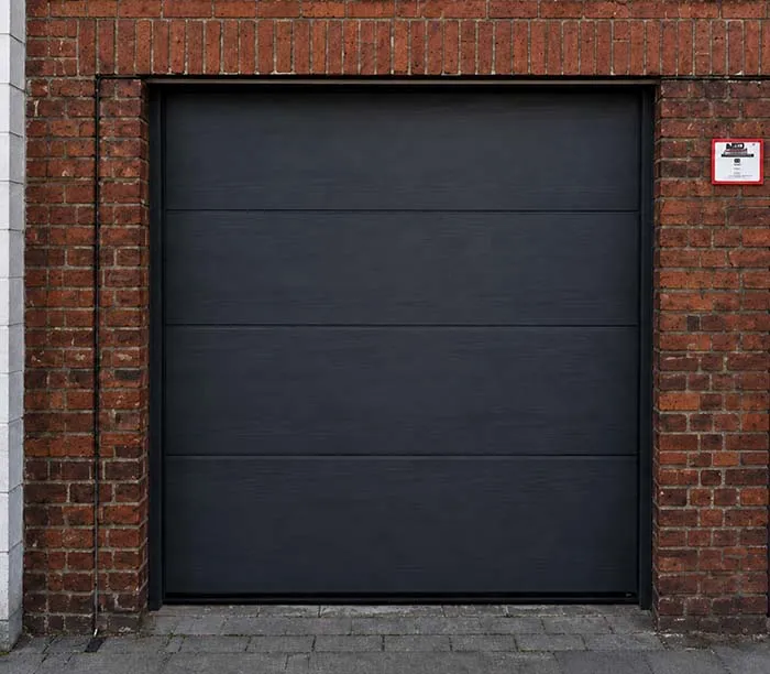 Porte de garage noire moderne encadrée de briques rouges sur le mur d'une maison.