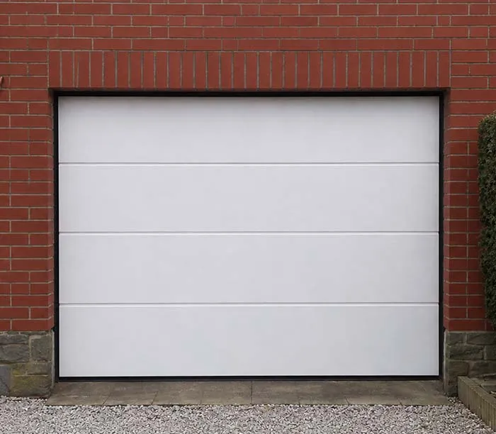 Porte de garage blanche moderne encadrée de briques rouges et pierres grises au sol.