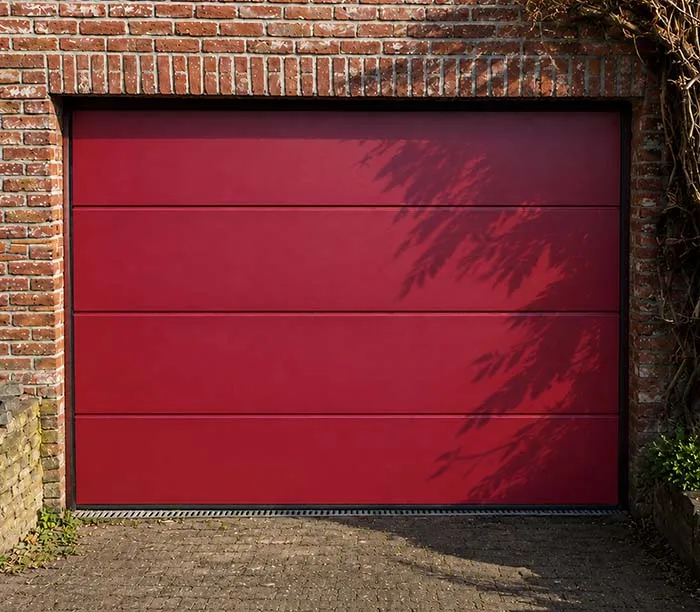 Porte de garage rouge moderne encadrée par un mur en briques sur une allée pavée.