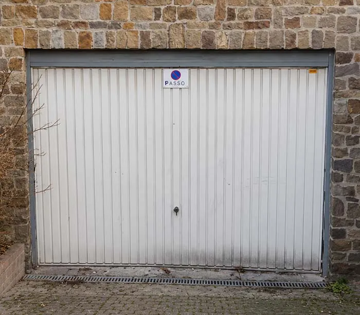 Porte de garage blanche avec un panneau « Passo » fixée sur un mur en pierre.