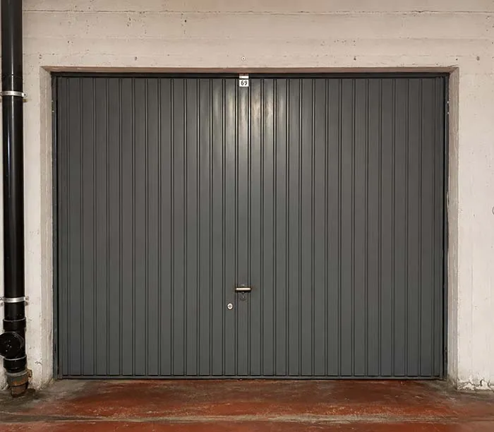 Porte de garage grise en métal avec poignée et numéro 69 au-dessus dans un mur en béton.