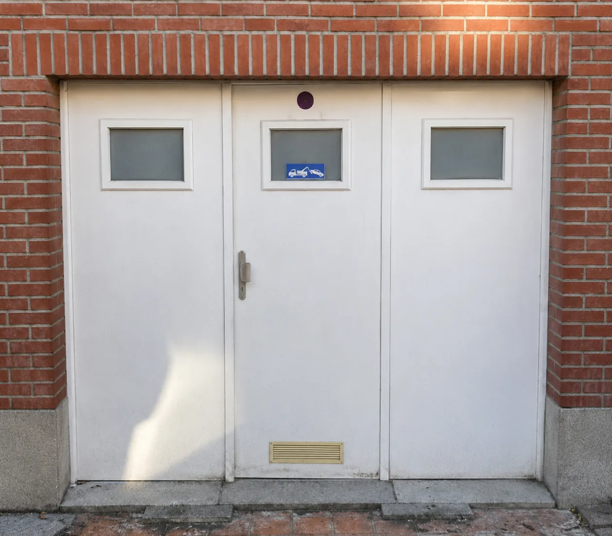 Porte blanche avec trois fenêtres carrées et un panneau bleu indiquant une zone de remorquage.