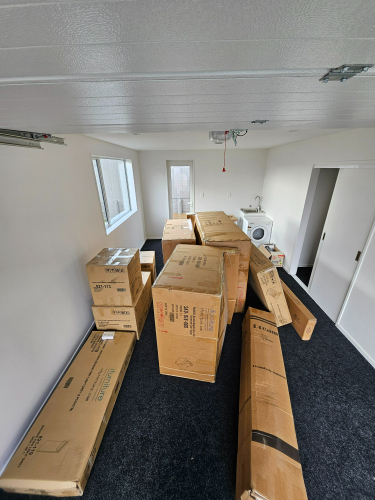 A room with several large cardboard boxes stacked and a washing machine in the background.