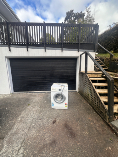 Washing machine on concrete surface near garage door and stairs.