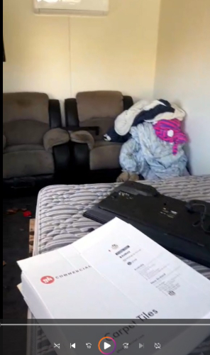 Two recliner chairs, a pile of blankets and clothing, a bed with a striped mattress, a black laptop, and a document folder.