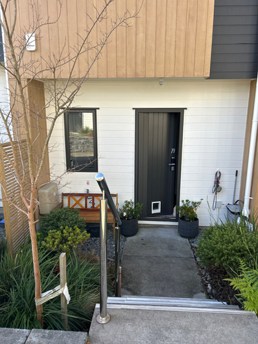 Front door with a pet door, potted plants, and a wooden bench.