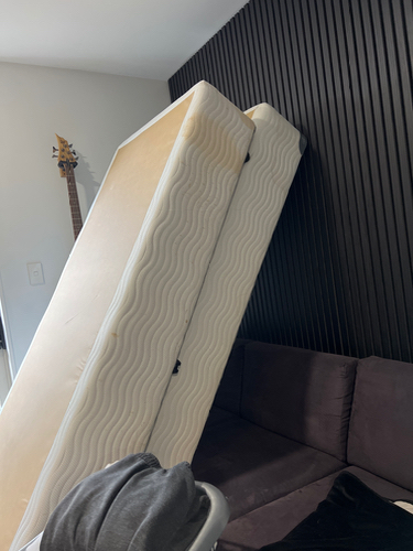 Stacked mattresses leaning against a wall, with a gray sweater on a couch and a guitar in the background.