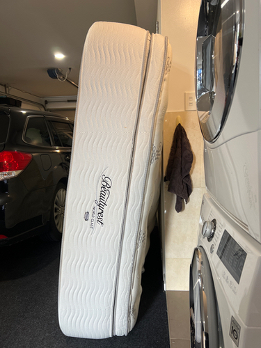 Mattress leaning against a wall, washing machine and dryer in background.