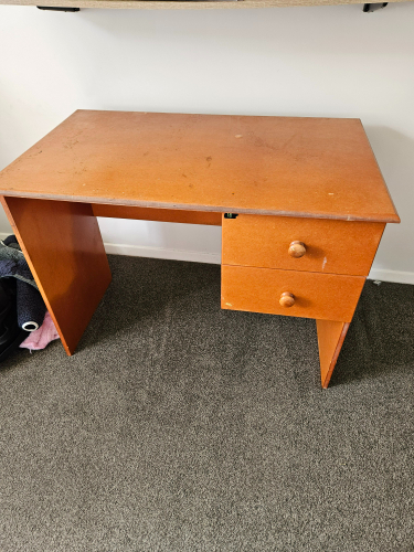 Wooden desk with two drawers, one with a round handle, and a flat surface.