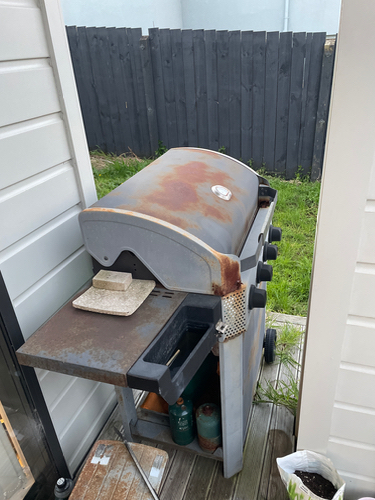 Rusty gas grill with side shelf and propane tanks.
