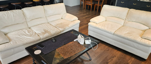 Two cream-colored sofas and a coffee table with a black runner, a coaster, a decorative mat, a remote control, a notebook, and a phone.