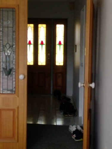 Double wooden doors with stained glass featuring red roses, a tiled floor, and various pairs of shoes.