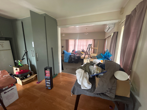 Interior room with a refrigerator, a table covered in items, storage boxes, and curtains.