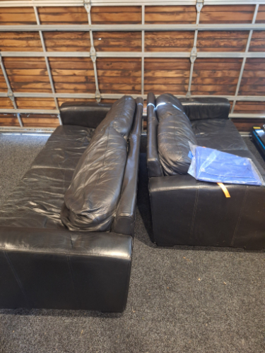 Two black leather sofas with a blue blanket on one of them.