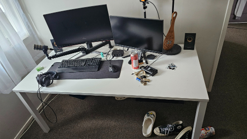 Desk with two monitors, keyboard, mouse, headphones, microphone, decorative vase, speakers, soda can, and keys.