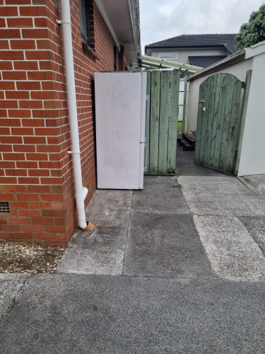 White refrigerator next to a wooden gate.