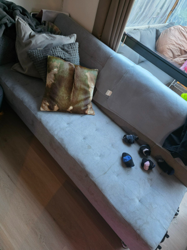 Gray couch with a patterned pillow and several small objects, including two black socks and two colored bands.