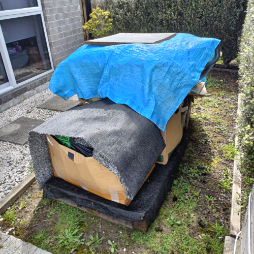 A cardboard box covered with a blue tarp and a black mat.