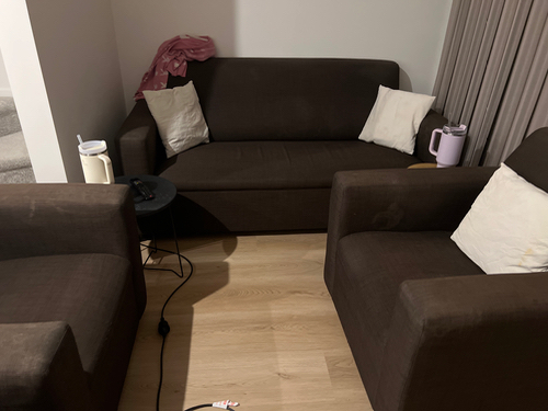 Two brown sofas with white throw pillows, a small black side table, a pink pitcher, and a white pitcher.