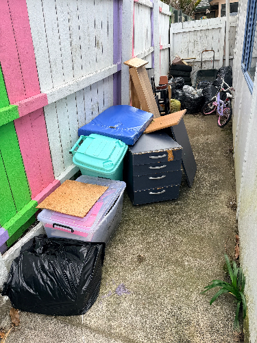 Bags of trash, plastic bins, stacked furniture, a bicycle, and wooden boards.
