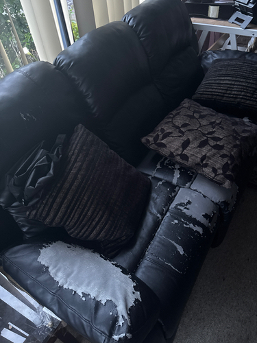 Black leather couch with worn areas and decorative pillows.