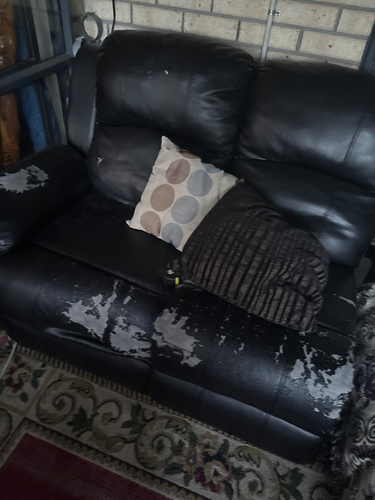 Black leather couch with wear and tear, patterned throw pillow, and a brown striped pillow.