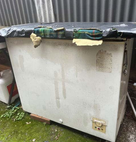 Old chest freezer with a damaged lid covered in fabric.