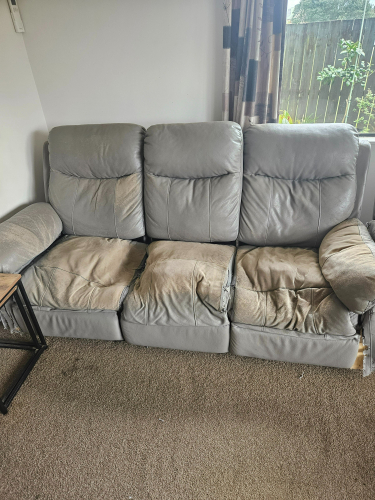 Gray recliner sofa with worn and torn cushions.