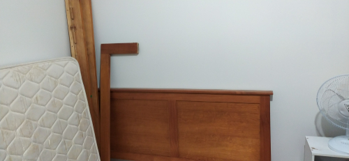 Wooden bed frame, mattress, standing fan, wooden headboard.