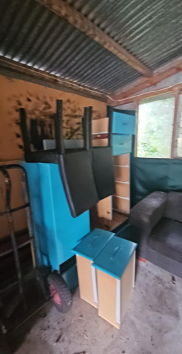 Blue cart with red wheel, stacked blue and black furniture, beige drawer unit, dark sofa.