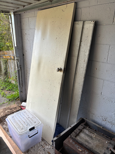 White door leaning against a wall, metal sheet, clear storage bin.
