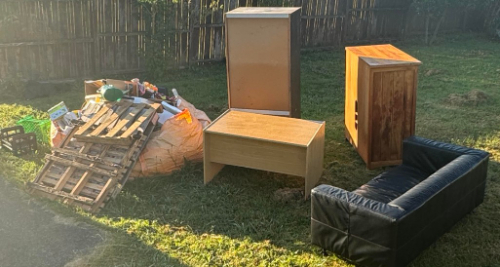 A wooden table, a wooden cabinet, a black leather sofa, a wooden box, a refrigerator, and a pile of garbage.