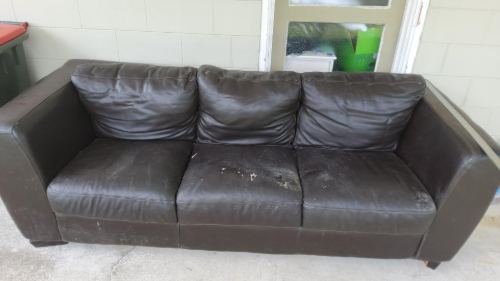 Brown leather couch with three cushions and visible wear.