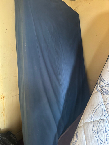 Blue mattress leaning against a wall, partially obscured by another mattress.