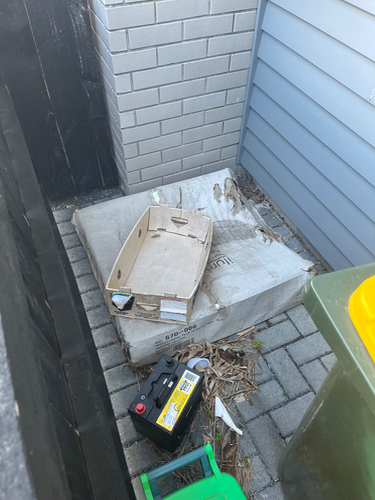Cardboard box, dirty mattress, car battery, green trash bin, yellow trash bin.