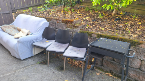 Sofa with blanket, three black chairs with cushions, small barbecue grill.