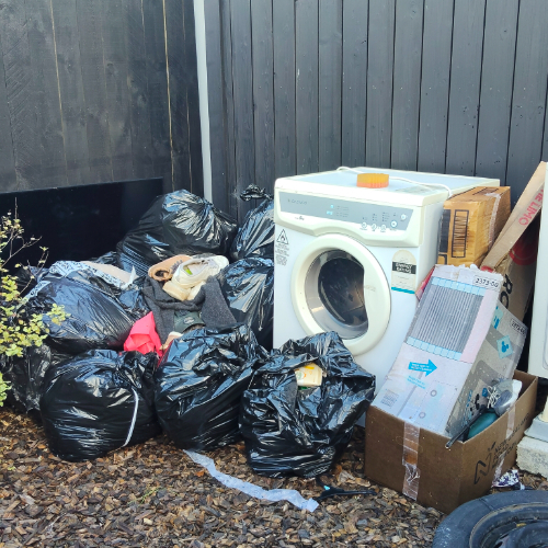 Washing machine next to black garbage bags and cardboard boxes.