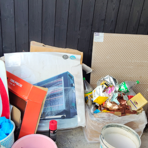 Boxed heater, cardboard boxes, trash bags with assorted waste, pink bucket, paint can, spray can.