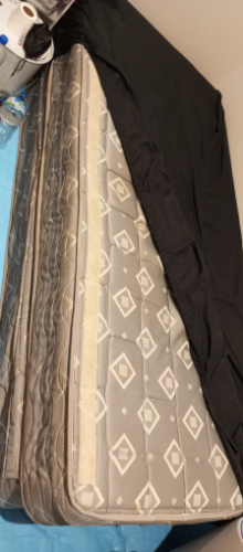Gray patterned mattress partially covered with a black fitted sheet.