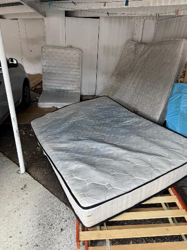 Two mattresses, one flat and one propped upright, on a wooden pallet.